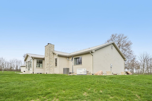 back of property featuring a lawn, a chimney, metal roof, and central AC