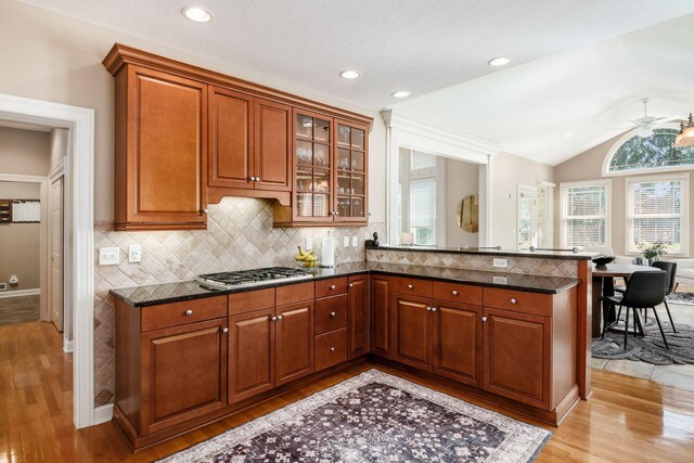 4568 Hickory Rock Dr, Powell, OH 43065 - kitchen featuring dark stone counters, stainless steel gas stovetop, light wood-style floors, glass insert cabinets, and backsplash