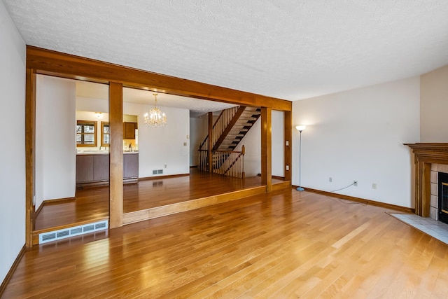 unfurnished living room featuring stairs, visible vents, light wood-style floors, and a chandelier