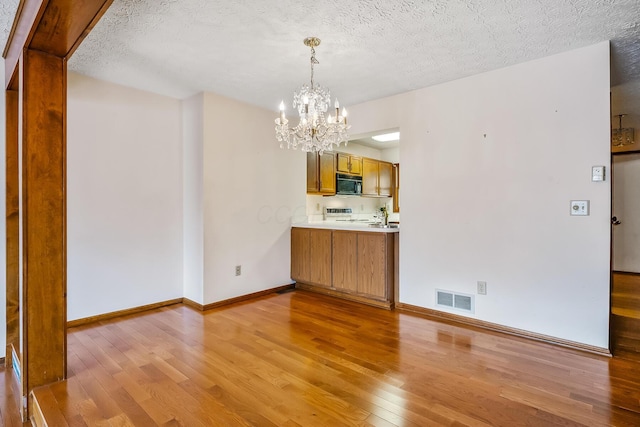 unfurnished dining area with a textured ceiling, visible vents, light wood finished floors, baseboards, and a notable chandelier
