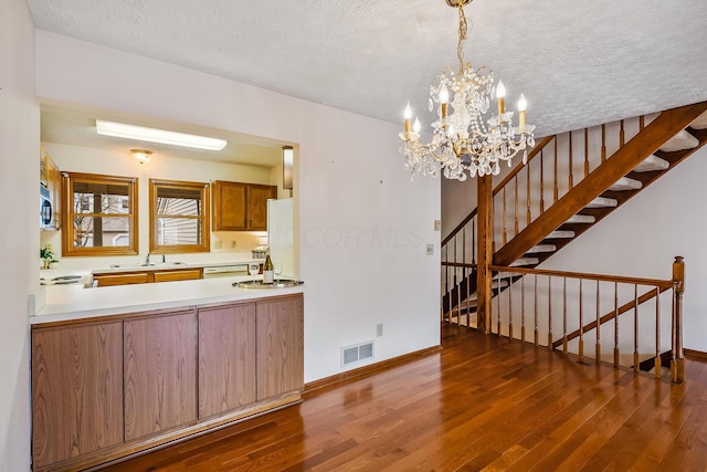 kitchen with a notable chandelier, wood finished floors, a textured ceiling, stainless steel microwave, and visible vents