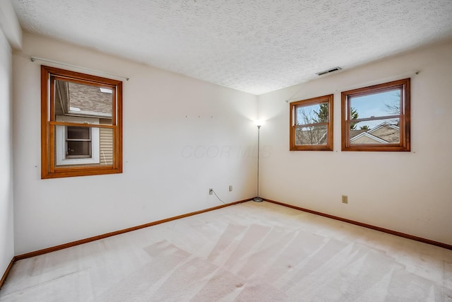 spare room with light carpet, baseboards, visible vents, and a textured ceiling