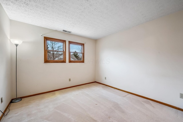 unfurnished room with light colored carpet, visible vents, baseboards, and a textured ceiling