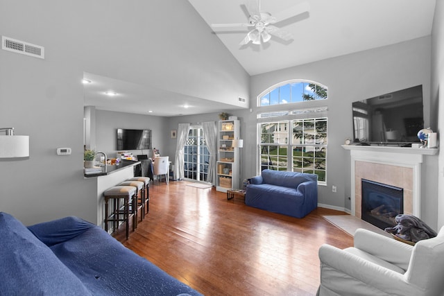 living room featuring ceiling fan, high vaulted ceiling, visible vents, a tile fireplace, and hardwood / wood-style flooring