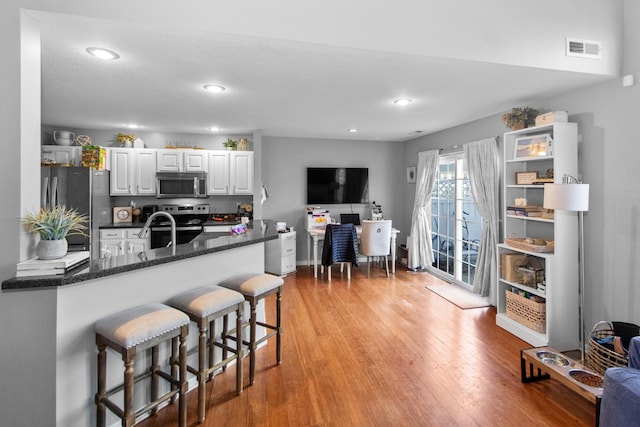 kitchen featuring light wood-type flooring, a breakfast bar, white cabinets, visible vents, and stainless steel appliances