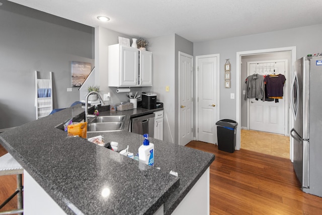 kitchen with a peninsula, white cabinetry, stainless steel appliances, a sink, and wood finished floors