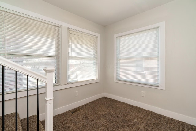 spare room featuring visible vents, dark colored carpet, and baseboards