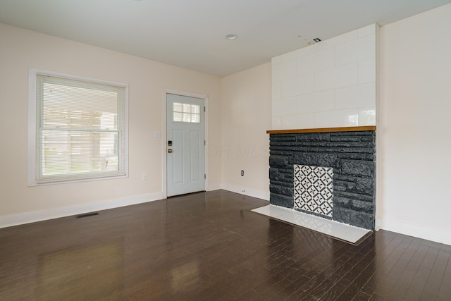 unfurnished living room with a stone fireplace, visible vents, baseboards, and dark wood-style flooring