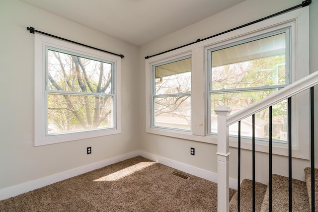 carpeted spare room with stairway, baseboards, a healthy amount of sunlight, and visible vents