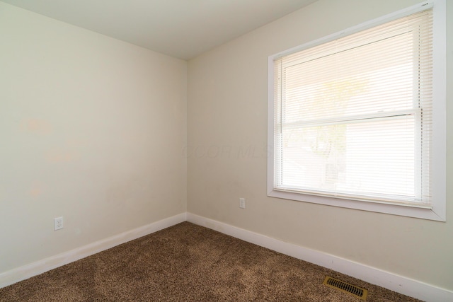 empty room featuring dark carpet, baseboards, and visible vents