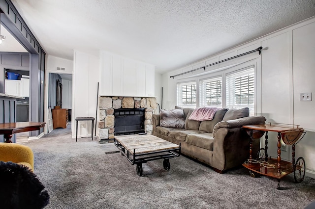 carpeted living area with a textured ceiling, visible vents, and a stone fireplace