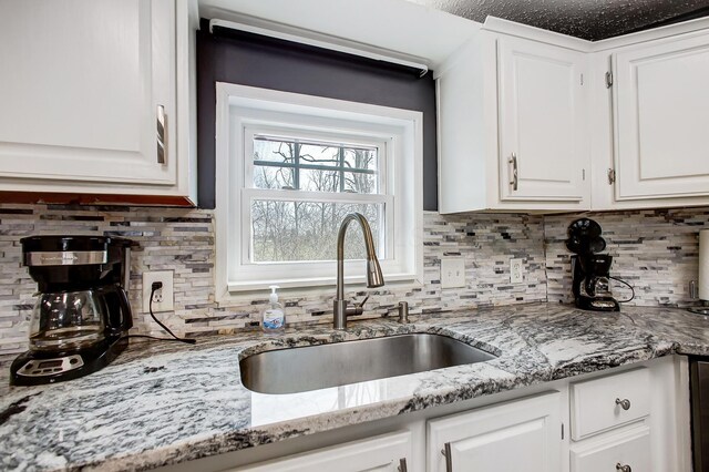 kitchen featuring white cabinets, a sink, tasteful backsplash, and light stone counters