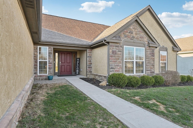 property entrance featuring a lawn, stucco siding, stone siding, and roof with shingles