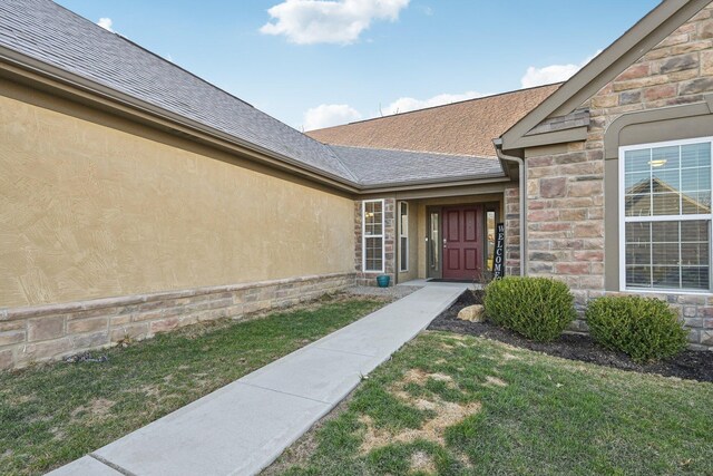 property entrance featuring a lawn, stucco siding, stone siding, and roof with shingles