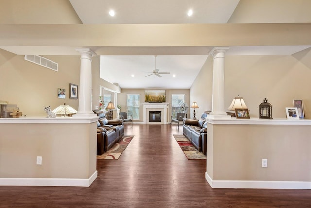 living area featuring ornate columns, dark wood finished floors, visible vents, a glass covered fireplace, and ceiling fan
