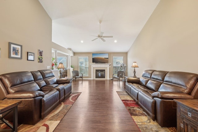 living room with high vaulted ceiling, wood finished floors, a glass covered fireplace, ceiling fan, and ornate columns
