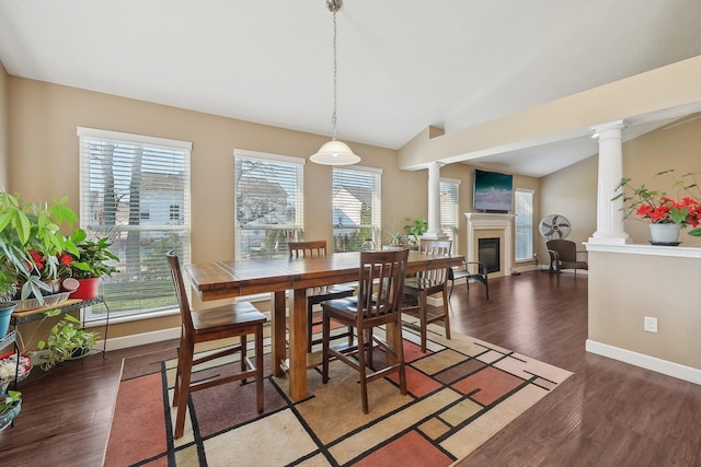 dining room featuring decorative columns, wood finished floors, lofted ceiling, and a glass covered fireplace