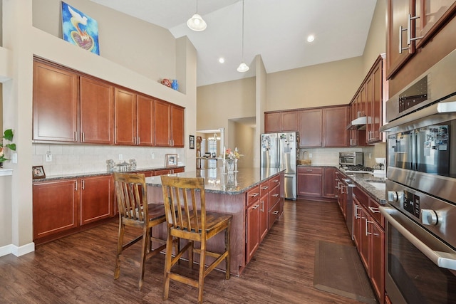 kitchen featuring dark wood-style flooring, a center island, high vaulted ceiling, dark stone countertops, and appliances with stainless steel finishes