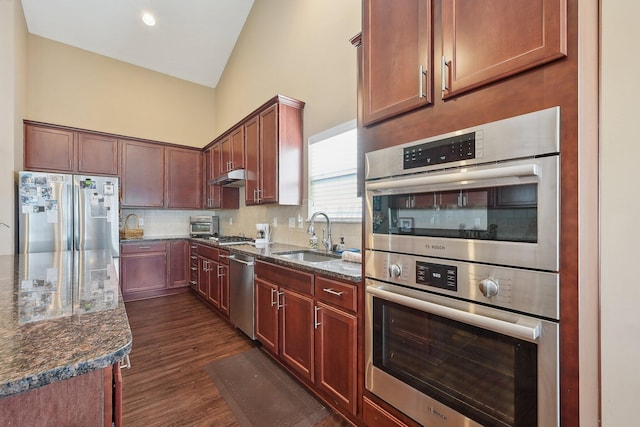 kitchen with dark stone counters, stainless steel appliances, tasteful backsplash, under cabinet range hood, and a sink