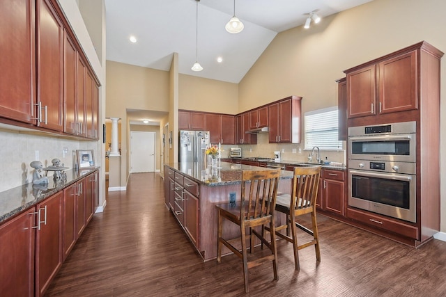 kitchen with stainless steel appliances, dark wood-type flooring, under cabinet range hood, dark stone countertops, and a kitchen island