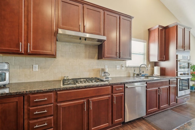 kitchen with decorative backsplash, stainless steel appliances, dark wood-type flooring, under cabinet range hood, and a sink