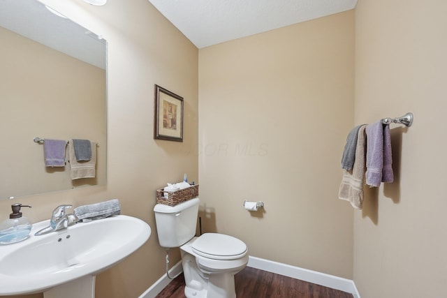half bathroom with baseboards, wood finished floors, toilet, and a sink