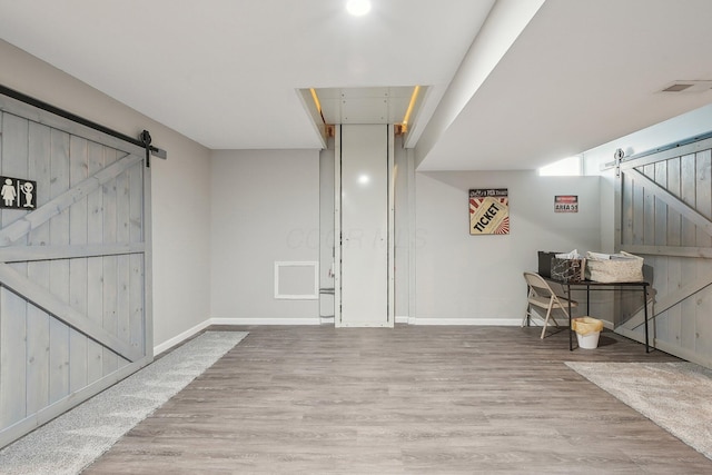 basement featuring baseboards, a barn door, and wood finished floors
