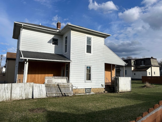 rear view of house with a lawn, a chimney, and fence