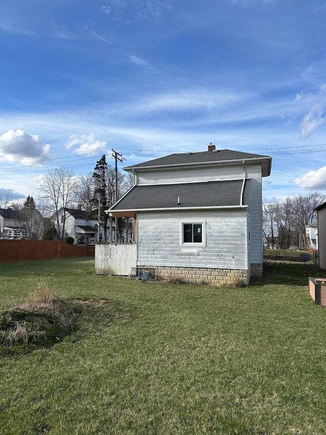 back of property featuring a lawn, a shingled roof, and fence