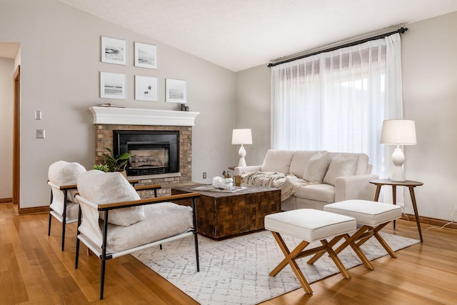 living area featuring lofted ceiling, light wood-style flooring, baseboards, and a brick fireplace