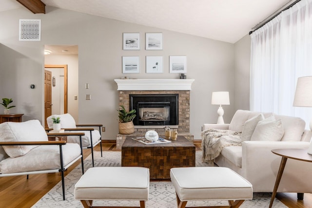 living room with lofted ceiling with beams, light wood finished floors, baseboards, visible vents, and a fireplace