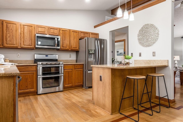 kitchen featuring brown cabinets, light wood-style floors, stainless steel appliances, a peninsula, and light stone countertops