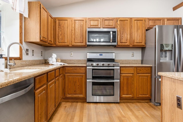 kitchen featuring brown cabinets, lofted ceiling, stainless steel appliances, a sink, and light wood-style floors