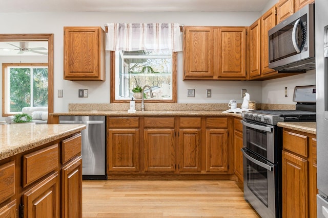 kitchen with light wood-style flooring, a sink, a ceiling fan, brown cabinets, and appliances with stainless steel finishes