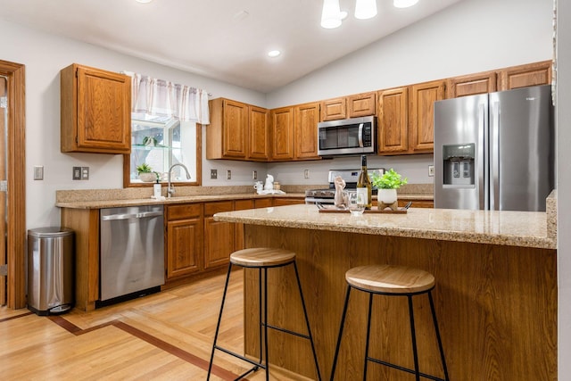 kitchen featuring brown cabinets, light stone counters, stainless steel appliances, a kitchen bar, and light wood-style flooring