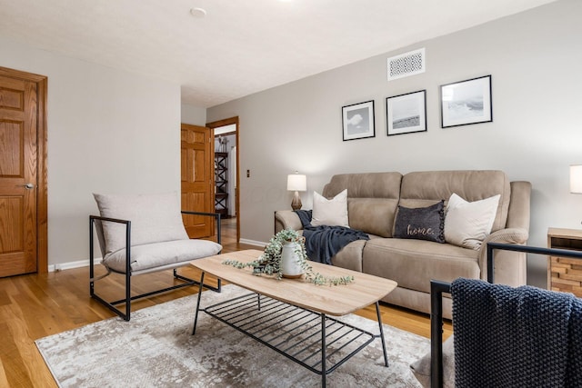 living room with light wood-style floors, visible vents, and baseboards