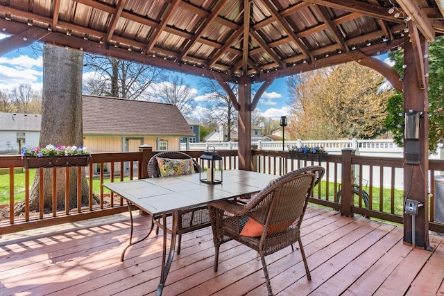 wooden deck with a gazebo, outdoor dining space, an outbuilding, and fence