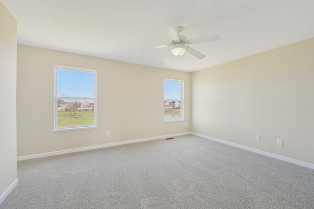 carpeted spare room with baseboards, ceiling fan, and visible vents