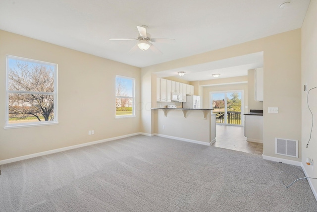 unfurnished living room with baseboards, a healthy amount of sunlight, light colored carpet, and visible vents