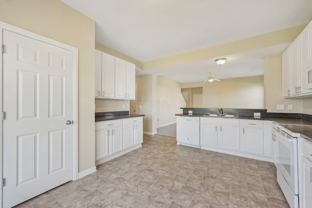 kitchen with a sink, a peninsula, white appliances, dark countertops, and white cabinets