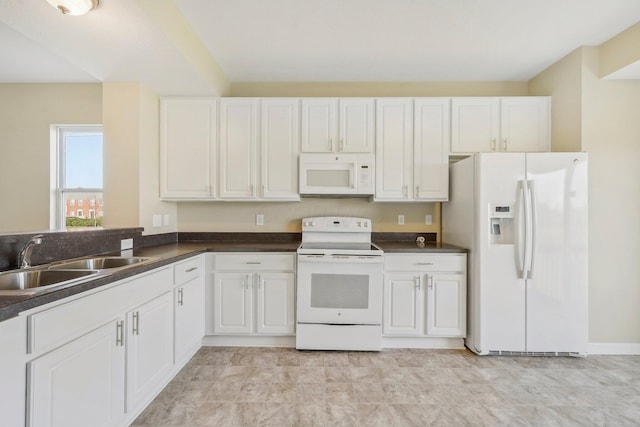 kitchen with white appliances, dark countertops, a sink, and white cabinetry