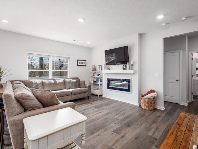 living room featuring baseboards, dark wood-style floors, a glass covered fireplace, and recessed lighting