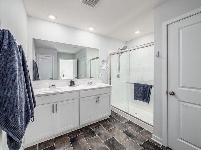 full bathroom with double vanity, a sink, a shower stall, and visible vents
