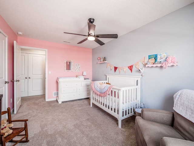 bedroom featuring carpet flooring, a crib, a ceiling fan, and a textured ceiling