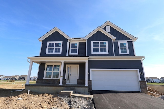 view of front of house with driveway, stone siding, covered porch, an attached garage, and board and batten siding