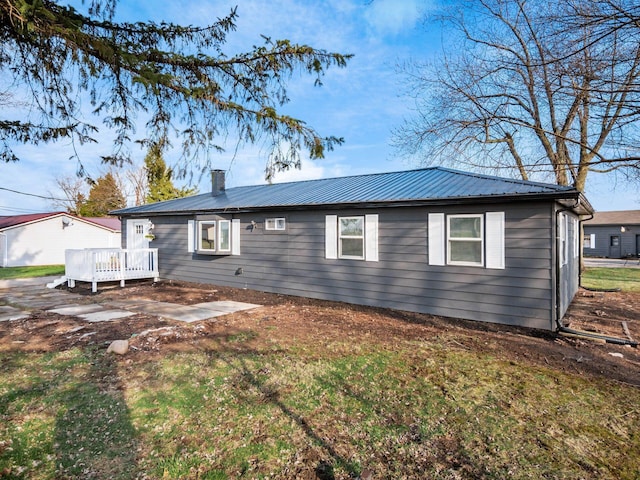 ranch-style house with a patio area, a chimney, a deck, a front lawn, and metal roof
