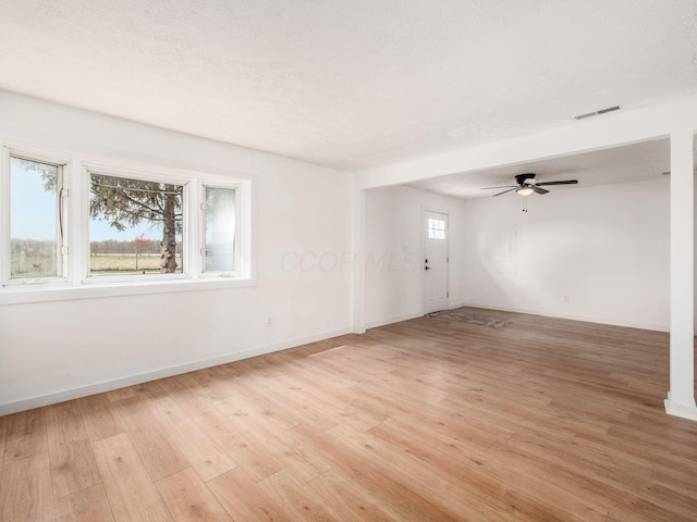 empty room featuring light wood finished floors, a textured ceiling, baseboards, visible vents, and ceiling fan