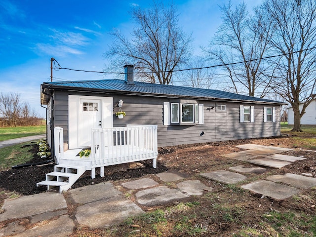 back of house with metal roof, a chimney, and a deck