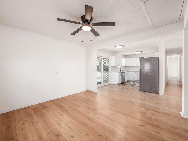unfurnished living room with light wood-style floors, ceiling fan, a sink, and a textured ceiling