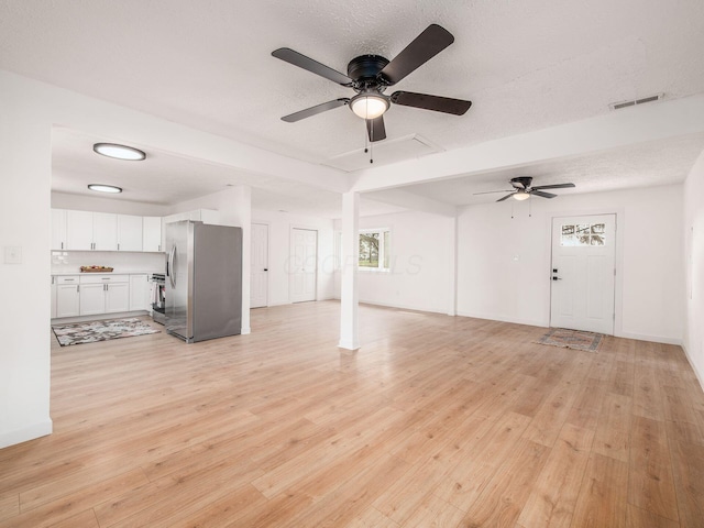 unfurnished living room featuring a textured ceiling, ceiling fan, visible vents, and light wood-style floors